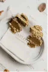 Par de aros colgantes dorados con cuatro dijes metálicos móviles con forma de hojas o gotas brillantes. Fabricados en acero quirúrgico con baño de oro.