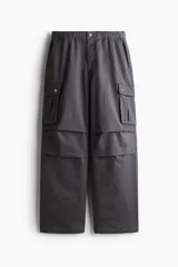 Pantalón cargo gris oscuro de corte holgado, con cintura elástica y bolsillos laterales, traseros y tipo cargo con solapa y botón a presión.