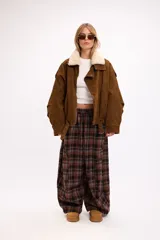 Pantalon de corte oversize y tiro medio, confeccionado en tela con estampado de cuadros en tonos marrones y negros. Presenta una silueta amplia y holgada con cintura elástica y cordón ajustable.