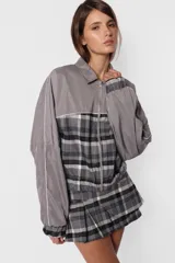Minifalda gris con estampado de cuadros escoceses, cintura ancha, tablas en la parte inferior y cierre metálico lateral. Incluye sobrefalda desmontable con bolsillo.