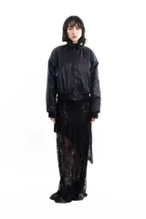Campera bomber negra de tela satinada con cierre frontal, cuello redondo y puños y cintura elastizados. Tiene un pequeño logo bordado en el pecho y un bolsillo con cierre en la manga. Es reversible.