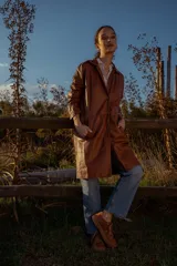 Gabardina marrón de cuero ovino italiano, con cuello camisero, cierre frontal con botones, mangas largas y corte recto.