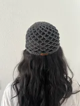 Gorro tipo casquete tejido a crochet con hilo satinado negro y etiqueta de cuero ecológico con logo de la marca.