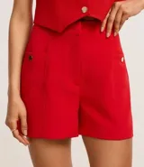 Short blanco de sastrería con cintura alta, bolsillos laterales con tachuelas metalizadas, recortes delanteros con costura aparente, bolsillos falsos y pinzas traseras.