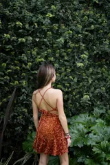 Vestido corto negro con estampado de hojas doradas, escote en V, breteles finos cruzados en la espalda, cut-outs laterales bajo el busto y volado en el ruedo.