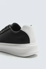 Zapatillas deportivas negras con detalle en blanco en el talón y suela blanca con volumen.