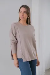 Sweater color beige de tejido de punto, corte recto y cuello redondo. Presenta detalle de botones decorativos en el hombro y lateral.
