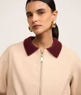 Campera bomber color beige con cuello y puños en color borgoña. Cierre frontal con cremallera y bolsillos laterales.