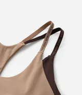 Top deportivo de microfibra ligera color beige con breteles dobles y espalda cruzada. Presenta detalle de lettering "Move Your Soul" en los breteles y abertura en la espalda.