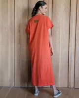 Vestido largo color crudo con cuello redondo y mangas cortas con ribete negro. Tiene corte recto y aberturas laterales en el ruedo.