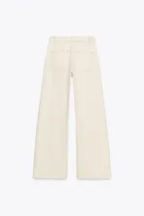 Pantalón de jean color crudo, de tiro alto y corte bootcut. Presenta cinturón fino del mismo tejido, bolsillos de parche en la parte trasera y cierre frontal con cremallera y botón.