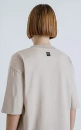 Remera color arena de corte crop y calce oversize, con hombros caídos y cuello redondo.