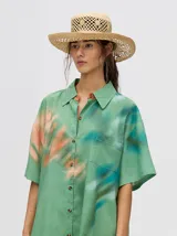 Camisa-vestido oversize de manga corta, color verde con estampado tie-dye en tonos salmón y turquesa. Presenta cuello camisero y cierre frontal de botones.