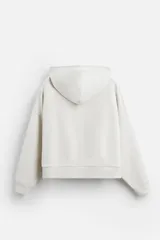 Sudadera color crudo, estilo hoodie, corte boxy, con capucha, manga larga, bolsillo tipo canguro y terminaciones en rib.
