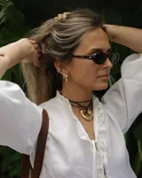 Collar con dije dorado irregular con agujero central, colgando de cordón negro ajustable.