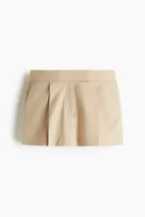 Short pollera corto color beige, de estilo sastre, con pinzas frontales, pretina prolongada con corchetes y bolsillos al bies.