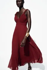Vestido midi color borgoña con escote en V, tirantes anchos con detalle de nudo y falda plisada. Cierre trasero con cremallera oculta.