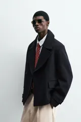 Abrigo corto azul marino de corte relajado, confeccionado en tejido con lana. Tiene cuello con solapas de pico, mangas largas con puños ajustables con trabilla, bolsillos de solapa en la cadera, bolsillo interior, abertura en el centro de la espalda y cierre frontal con botonadura.