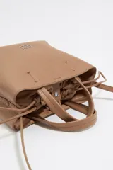 Bolso tote pequeño color visón de piel granulada con doble asa corta y correa bandolera ajustable y extraíble. Incluye bolsa interior ajustable con cordones. Logotipo de la marca grabado en el frente.