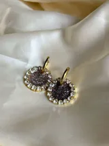 Par de aros colgantes con dije circular de resina con glitter multicolor y borde de strass. El arito es de acero quirúrgico dorado.