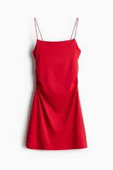 Vestido corto rojo de punto suave con escote cuadrado y breteles spaghetti. Diseño ajustado con frunces laterales y falda con leve vuelo.