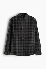 Camisa de popelina de algodón texturizado a cuadros negros y grises, de corte holgado, con cuello inglés, tapeta lisa, canesú con pliegue de caja en la espalda, mangas largas con abertura y cierre ajustable de botón en los puños, y bajo levemente redondeado.