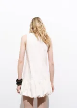 Vestido corto sin mangas de algodón estilo tejano vaquero, color blanco, con cuello redondo y bajo abullonado.