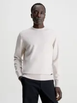 Sweater color beige de Calvin Klein, confeccionado en mezcla de tencel con elasticidad añadida. Tiene cuello redondo, puños y bajo de canalé, y etiqueta con logo de Calvin Klein por encima del bajo.