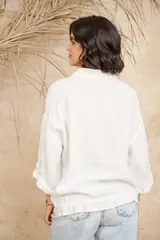 Camisa blanca de lino con cuello mao, mangas 3/4 con botón para sujetar, cierre con botones a tono y ajuste con cordón en la cintura.