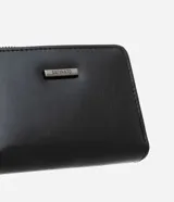Billetera pequeña de poliuretano color negro, con cierre de cremallera y botón a presión, espacio para tarjetas y logo metálico de la marca en el frente.