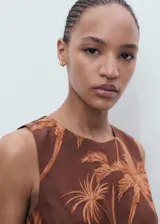 Mono largo sin mangas de color marrón con estampado de palmeras. Presenta un diseño con cuello redondo, detalle de nudo en la parte delantera y aberturas laterales tipo cut-out. Está confeccionado en una mezcla de lyocell y lino con forro de algodón, cuenta con perneras de corte recto y cierre de cremallera en la parte posterior.