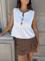 Top blanco sin mangas con cuello redondo y abertura frontal con lazos ajustables. Presenta textura de pliegues verticales en el frente.