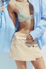 Falda pantalón color beige de tiro medio con diseño cruzado y cierre con botones. Cuenta con bolsillos falsos en la parte delantera y trasera, y cierre lateral con cremallera oculta.