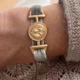 Pulsera con banda de terciopelo gris y apliques dorados con forma de moneda antigua.