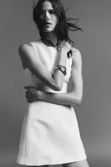 Vestido corto blanco de cuello redondo y sin mangas. Falda con pliegues y volumen. Cierre trasero con cremallera oculta.