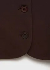 Chaleco marrón con cuello cuadrado, sin mangas, con cierre frontal de botones y dos bolsillos delanteros.