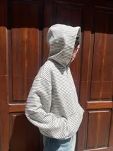 Campera con capucha y cierre frontal, color hueso con rayas finas horizontales en tono oscuro. Presenta un calce holgado (boxy fit) y puños y cintura acanalados.