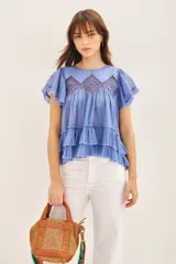 Camisa azul de algodón liviano con cuello redondo y gota en la espalda. Presenta detalle de bordado calado, terminación de volado en mangas y ruedo.