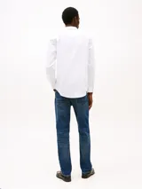 Camisa blanca de algodón con tecnología Flex, corte slim fit, cuello abotonado, mangas largas con puños redondeados y logo de Tommy Hilfiger bordado en el pecho.