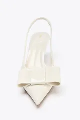 Zapato de tacón destalonado color blanco acharolado, con punta fina, lazo decorativo y tira trasera elástica.