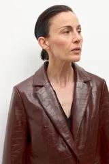 Blazer de corte recto, color marrón oscuro, con textura de eco cuero de cocodrilo. Presenta solapas de muesca, un solo botón frontal y bolsillos de ojal.