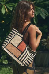 Bolso tipo tote de yute con diseño de bloques de color y rayas horizontales en negro y beige. Asas de hombro negras.