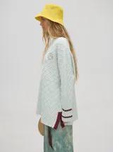 Sweater color crema con tejido en ochos, cuello redondo, puños acanalados con doble raya azul y tajos a los costados.