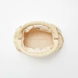 Bolso bandolera color beige, tejido en rafia con patrón de espiga. Tiene forma rectangular con cierre superior fruncido y cadena dorada para colgar al hombro.