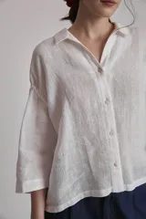 Camisa blanca de lino con cuello clásico, cierre frontal con botones y mangas 3/4 abullonadas.
