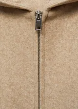 Chaqueta con capucha color beige, con cierre frontal de cremallera, cuello alto, puños elásticos y diseño oversize.