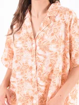 Camisa salmón con estampado de motivos marinos en blanco y marrón, de corte clásico, con cuello camisero, cierre frontal con botones y mangas cortas.