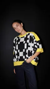Sweater de punto con mangas cortas, estampado geométrico en blanco y negro, y ribetes amarillos en cuello, puños y ruedo.