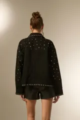 Campera de jean negra con tachas plateadas en el cuello, solapas y parte delantera. Tiene cierre asimétrico, bolsillos laterales con cierre y puños con cierre.