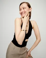 Pulsera rígida dorada de aleación de metales bañada en oro 18k, con dos cristales facetados grises en los extremos.